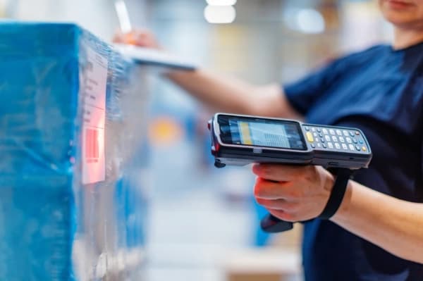 Worker using a handheld scanner to read a barcode on a blue wrapped shipping pallet.