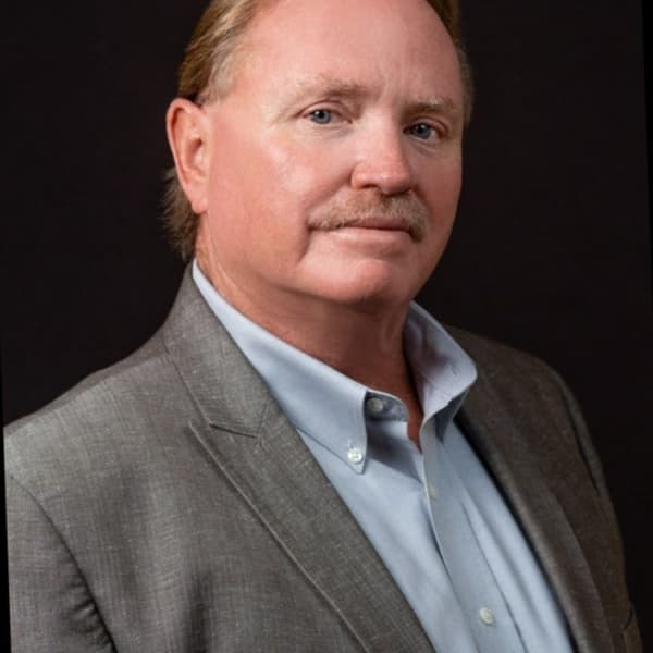 Middle-aged man with reddish hair and mustache, wearing a grey blazer and blue shirt.