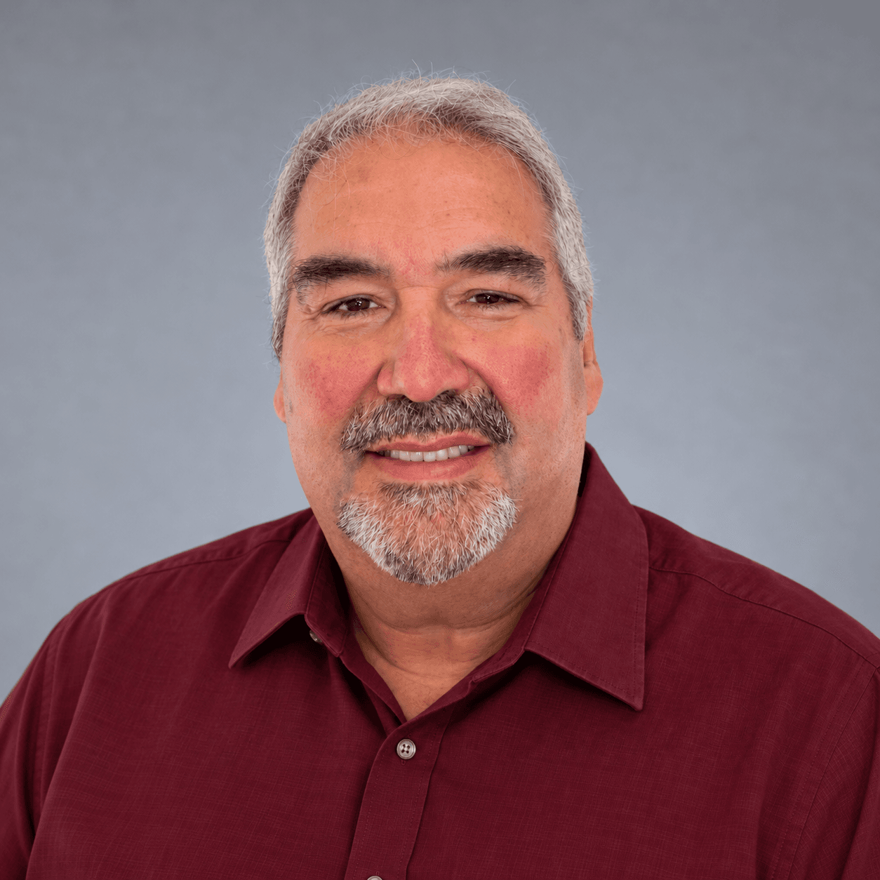 Smiling middle-aged man with gray hair and a goatee wearing a maroon button-down shirt.
