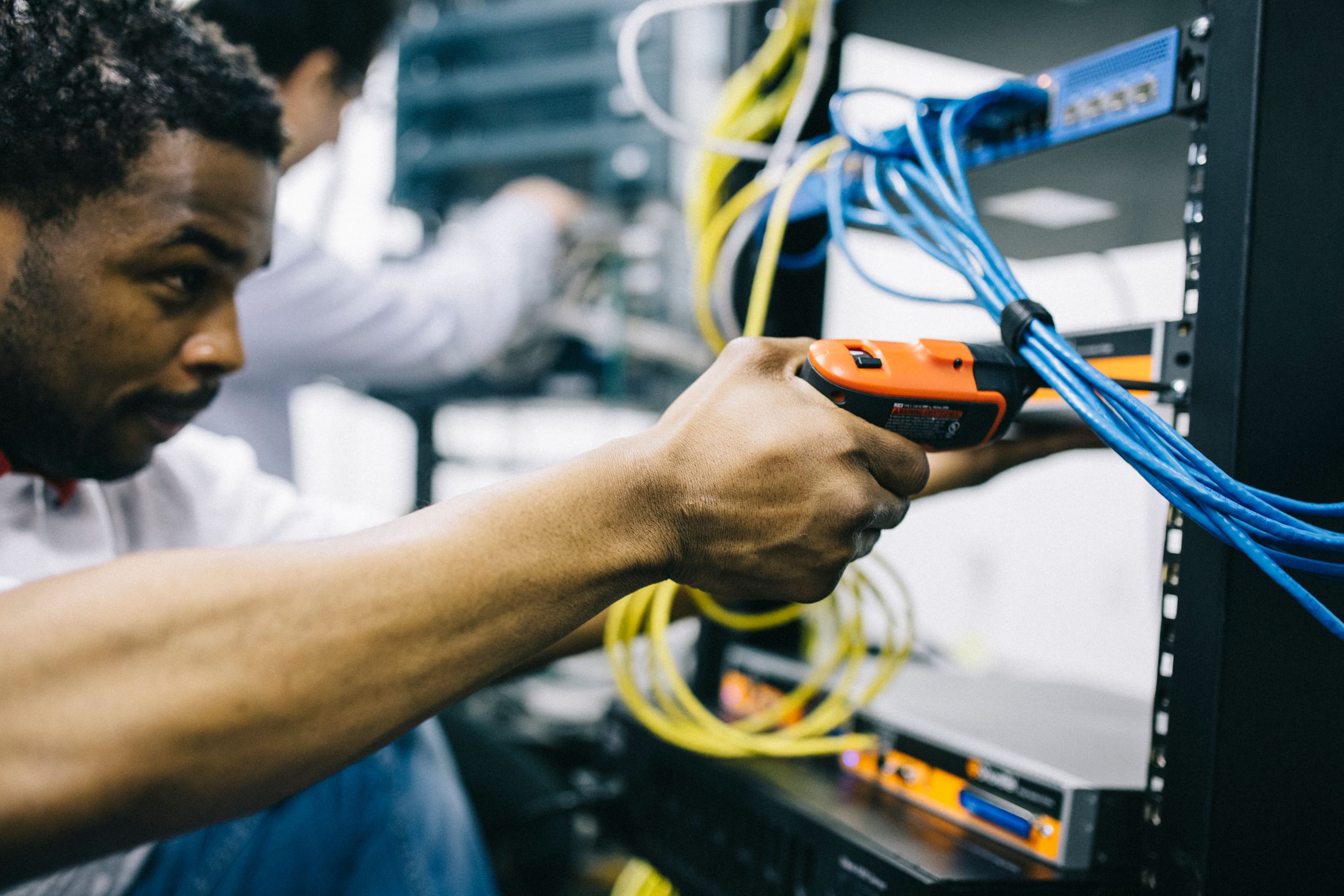 Technician using an orange power tool to work on a server rack with blue cables.