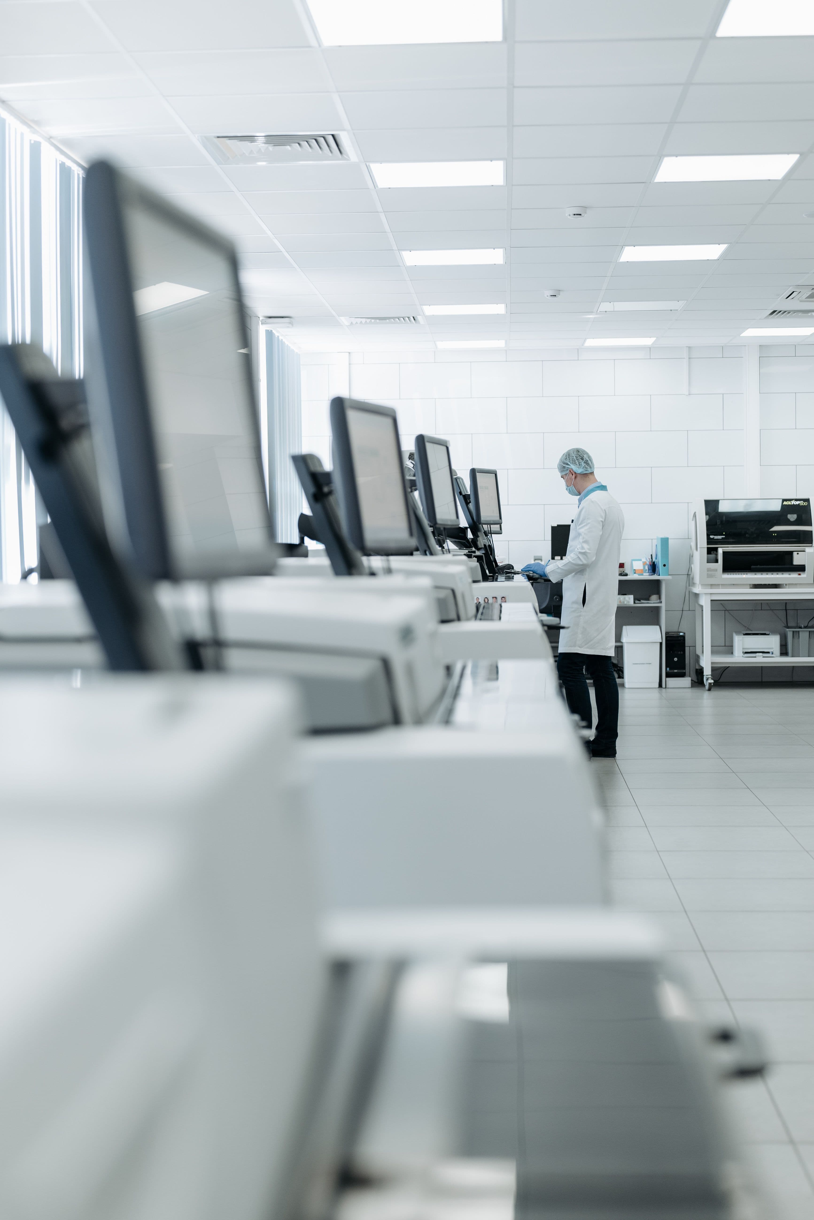 Scientist in protective gear working at a computer station in a bright, modern medical laboratory.