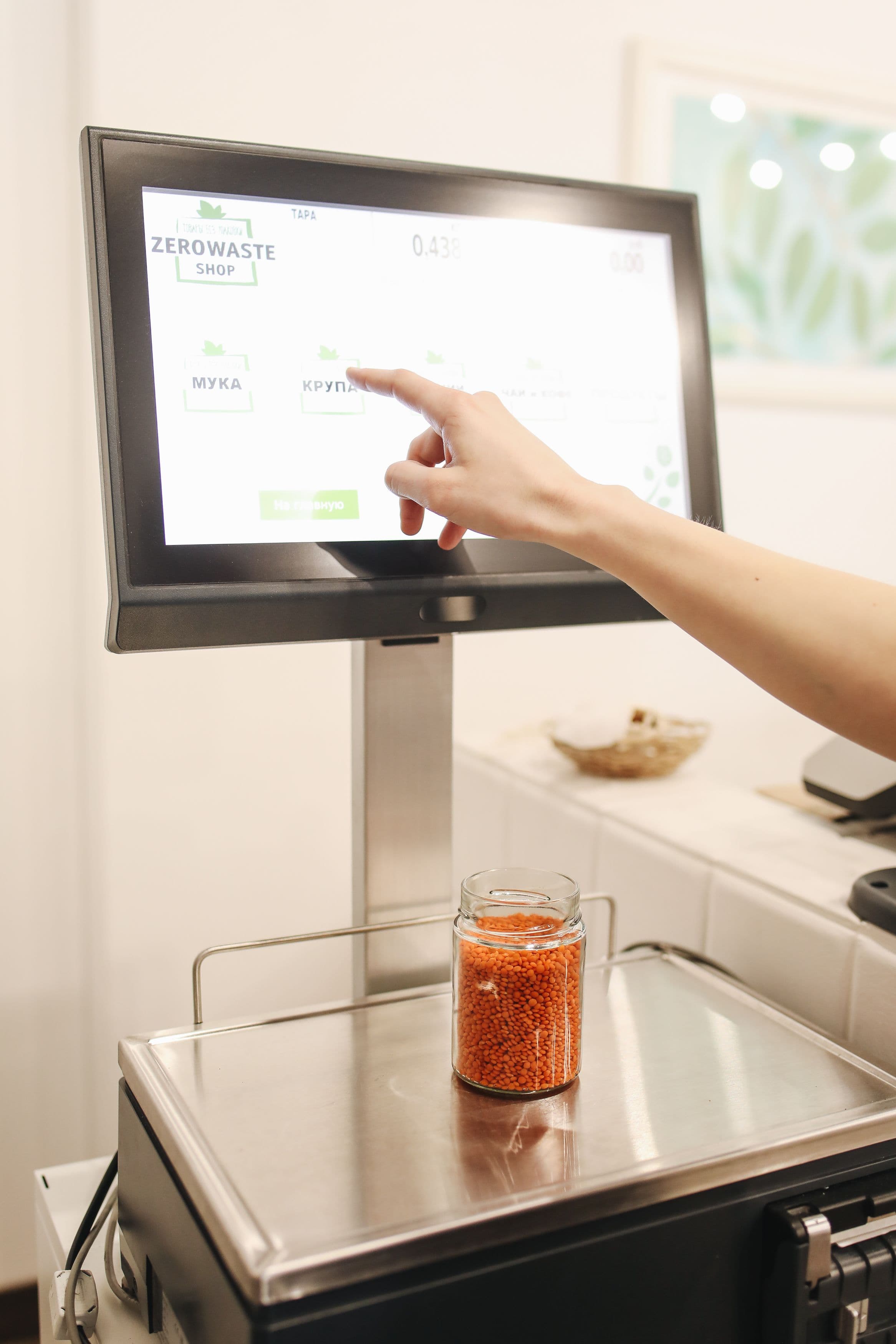 Hand touching a touchscreen scale to weigh a glass jar filled with red lentils.