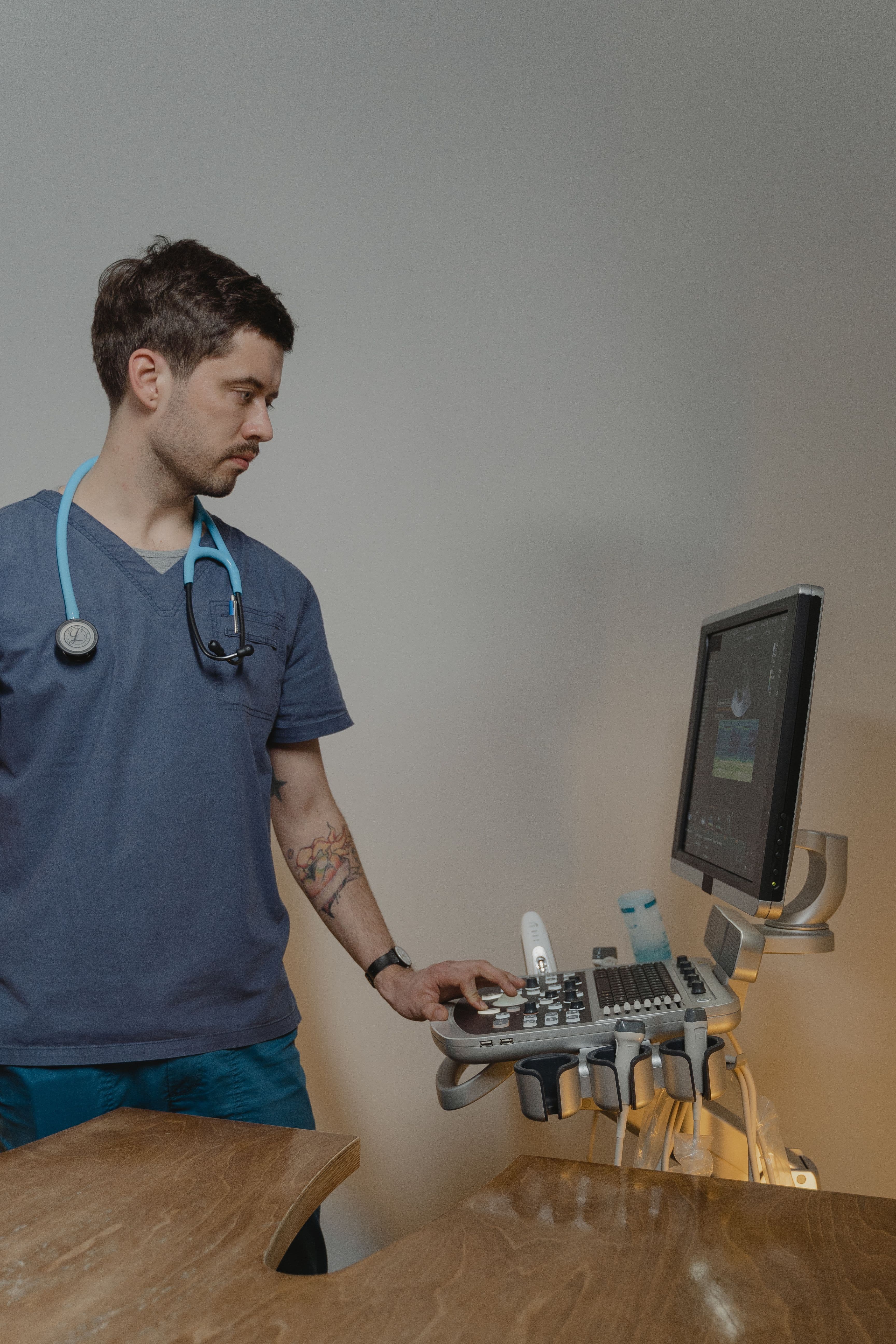 Male medical professional in blue scrubs operating an ultrasound machine and viewing the monitor.